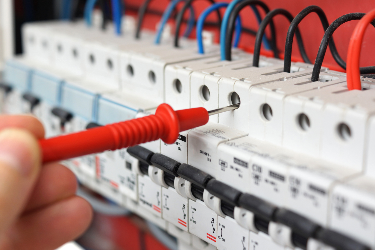 Hand of electrician with multimeter probe at electrical switchgear cabinet