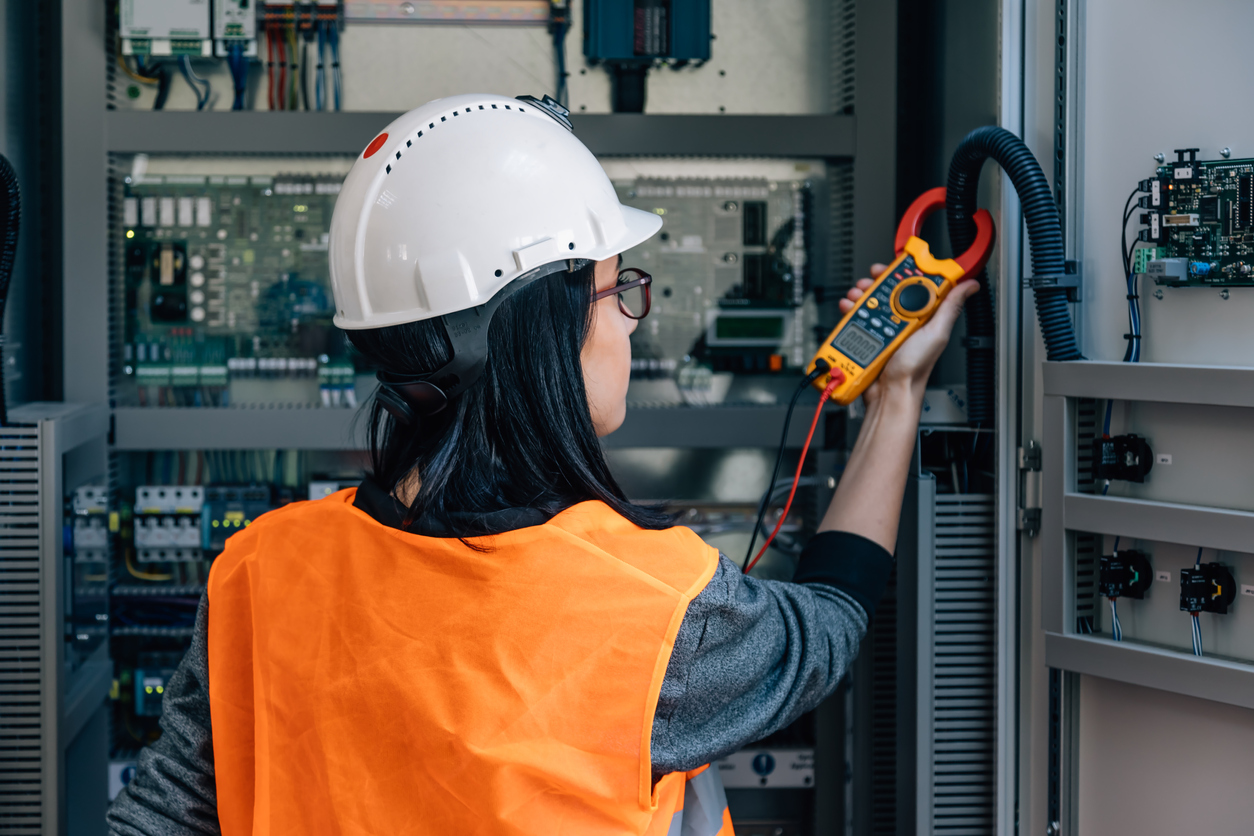 Young female maintenance engineer testing voltage with digital multimeter