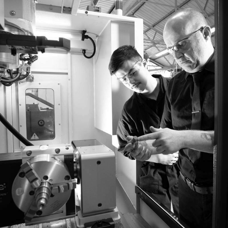 Male mentor helping Machinist apprentice use CNC machine