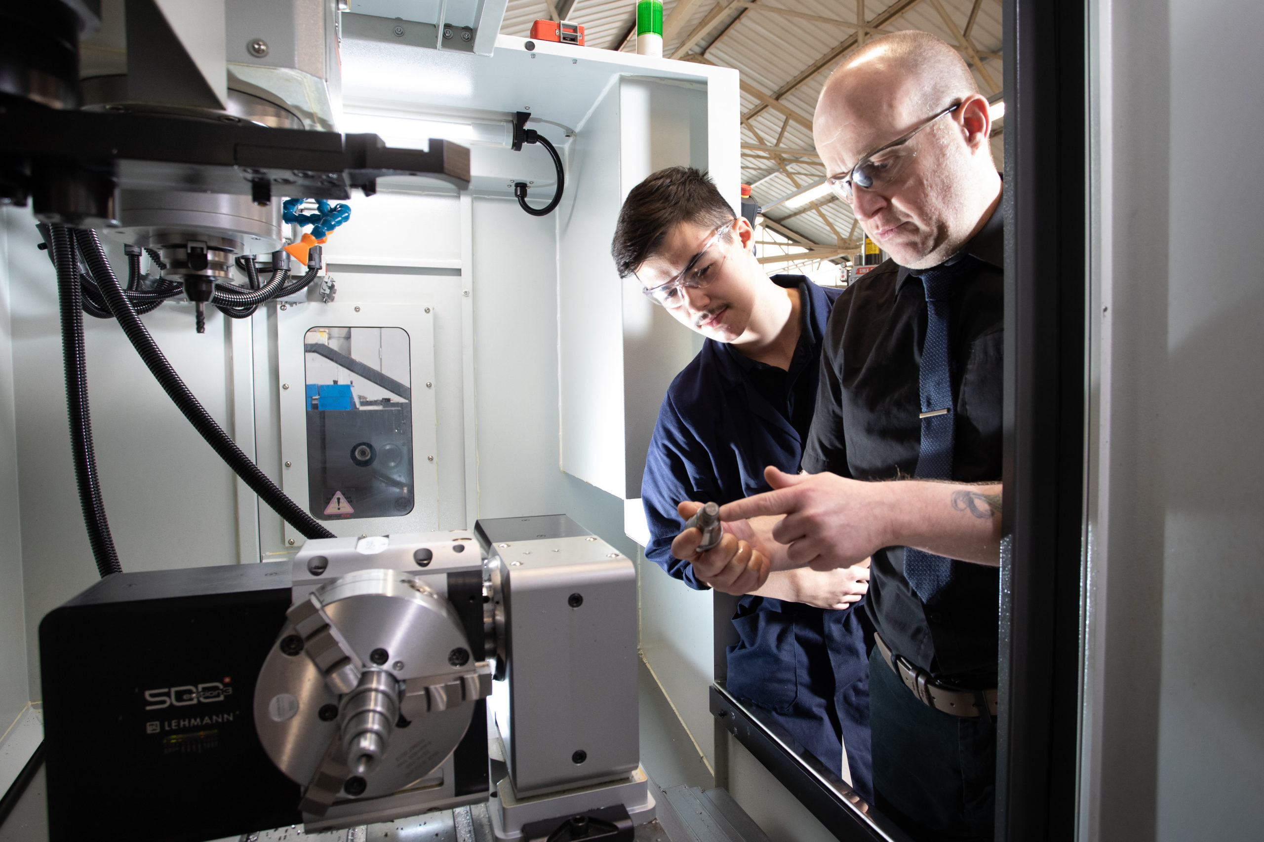 Male mentor helping Machinist apprentice use CNC machine