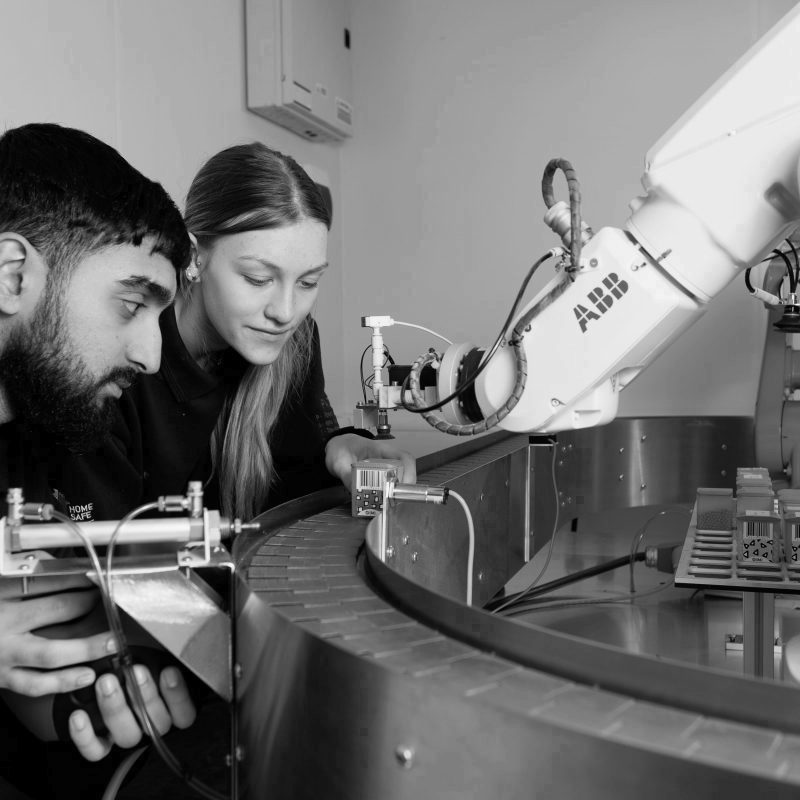 Male and female engineering apprentices operating an ABB robot