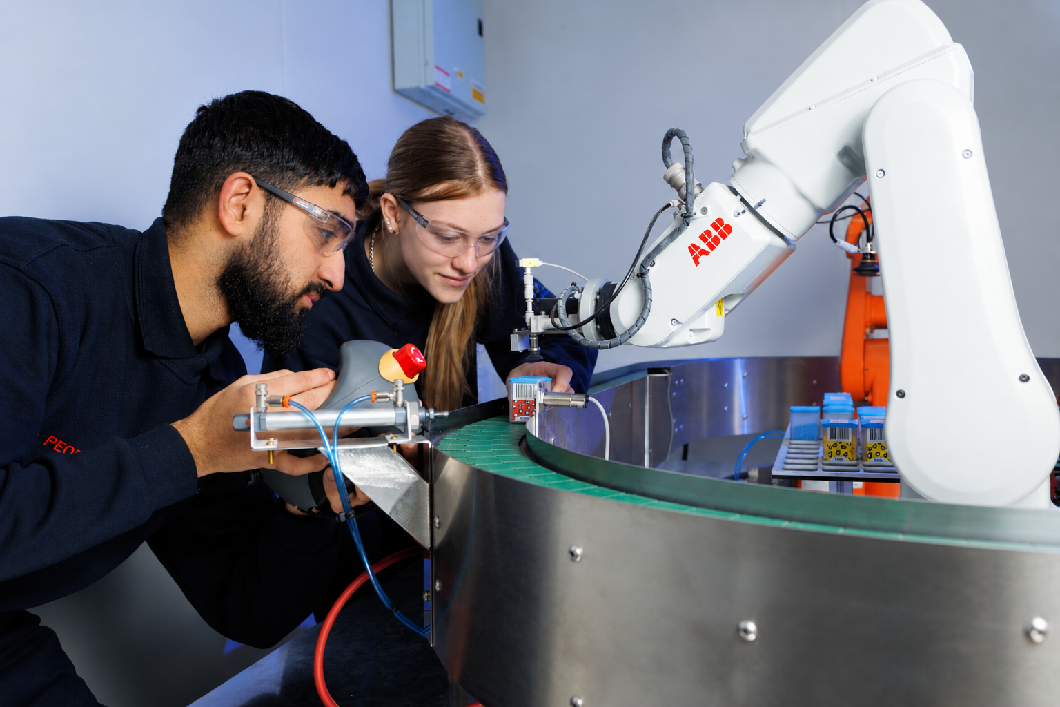 Male and female engineering apprentices wearing safety glasses operating an ABB robot within a training environment